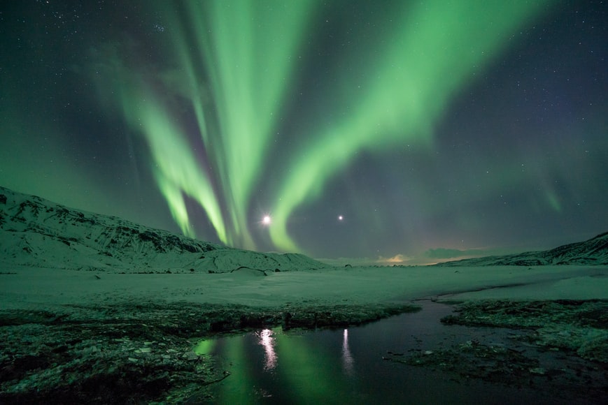 The Northern Lights dance over an snow-lined lagoon