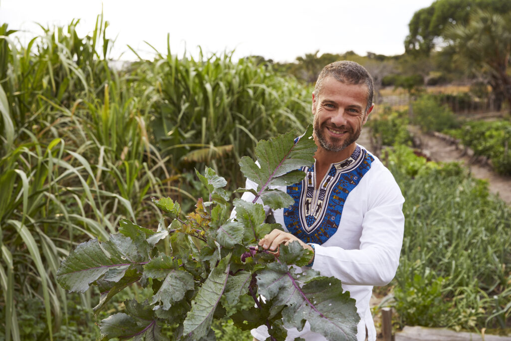 Joseph Moubayed, Head of Culinary at Kisawa Sanctuary, stands in the vegetable garden holding a leafy plant